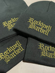 A pile of black hats with the words "Rockwell Barbell" in gothic letter font on the front of each one, in army green.