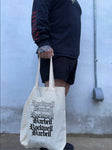 Person holding a tote bag with 'Rockwell Barbell' branding against a plain wall.