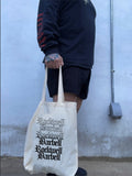 Person holding a tote bag with 'Rockwell Barbell' branding against a plain wall.