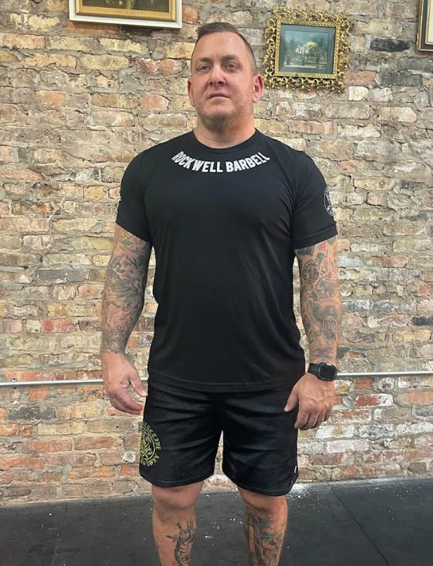 Matt wearing a Competition Shirt, facing the viewer. The words "Rockwell Barbell" can be seen at the top of the shirt in silver, near the neckline of the shirt.