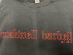 A detailed close up of the Established Crew crew shirt. The name "Rockwell Barbell" is shown in read, gothic outlibed letters. "Est 2014" is also in red letters under that text.